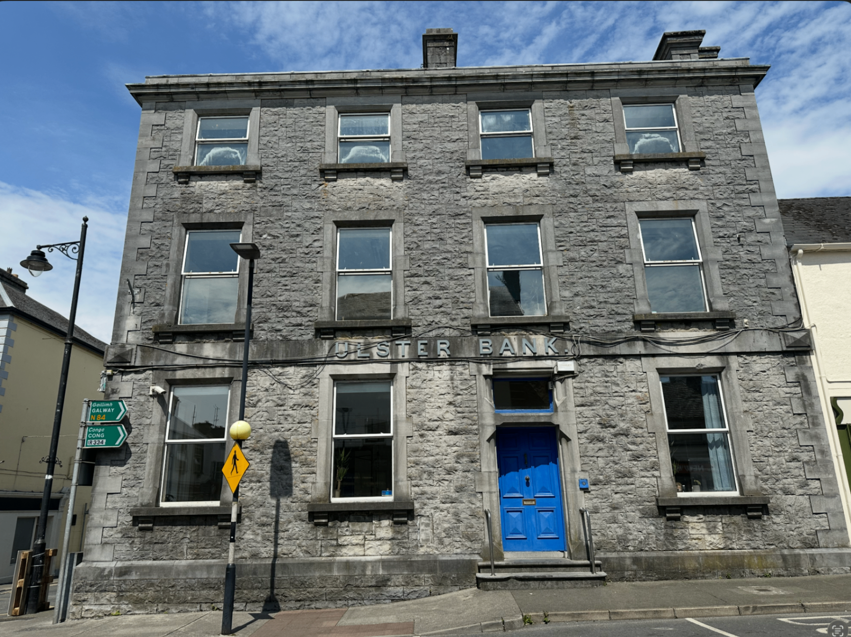 The former Ulster Bank building on Glebe Street, Ballinrobe, a three-storey cut-limestone Victorian banking house with a blue door